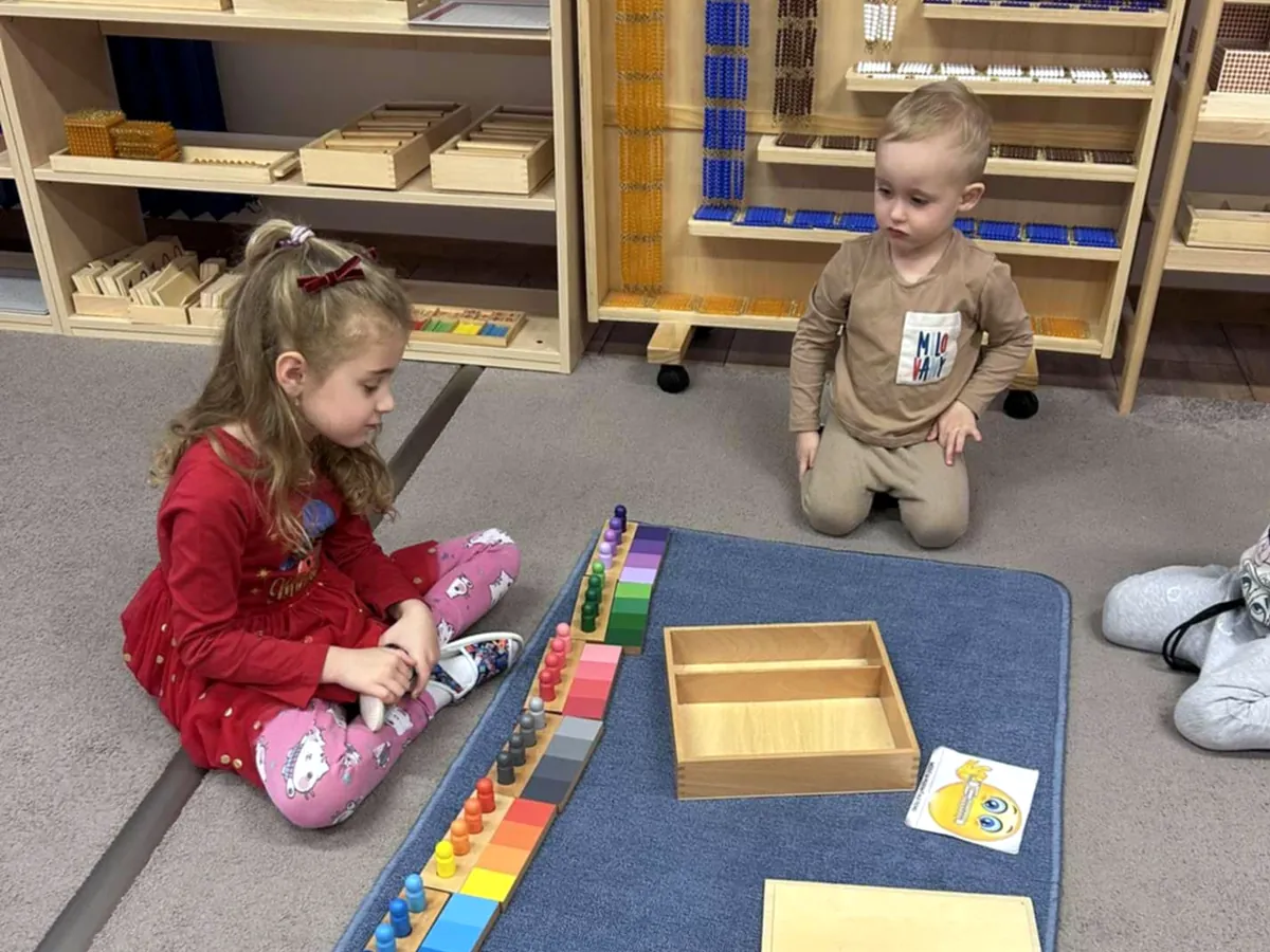 Deti sedia na koberci pred policami s Montessori pomôckami
