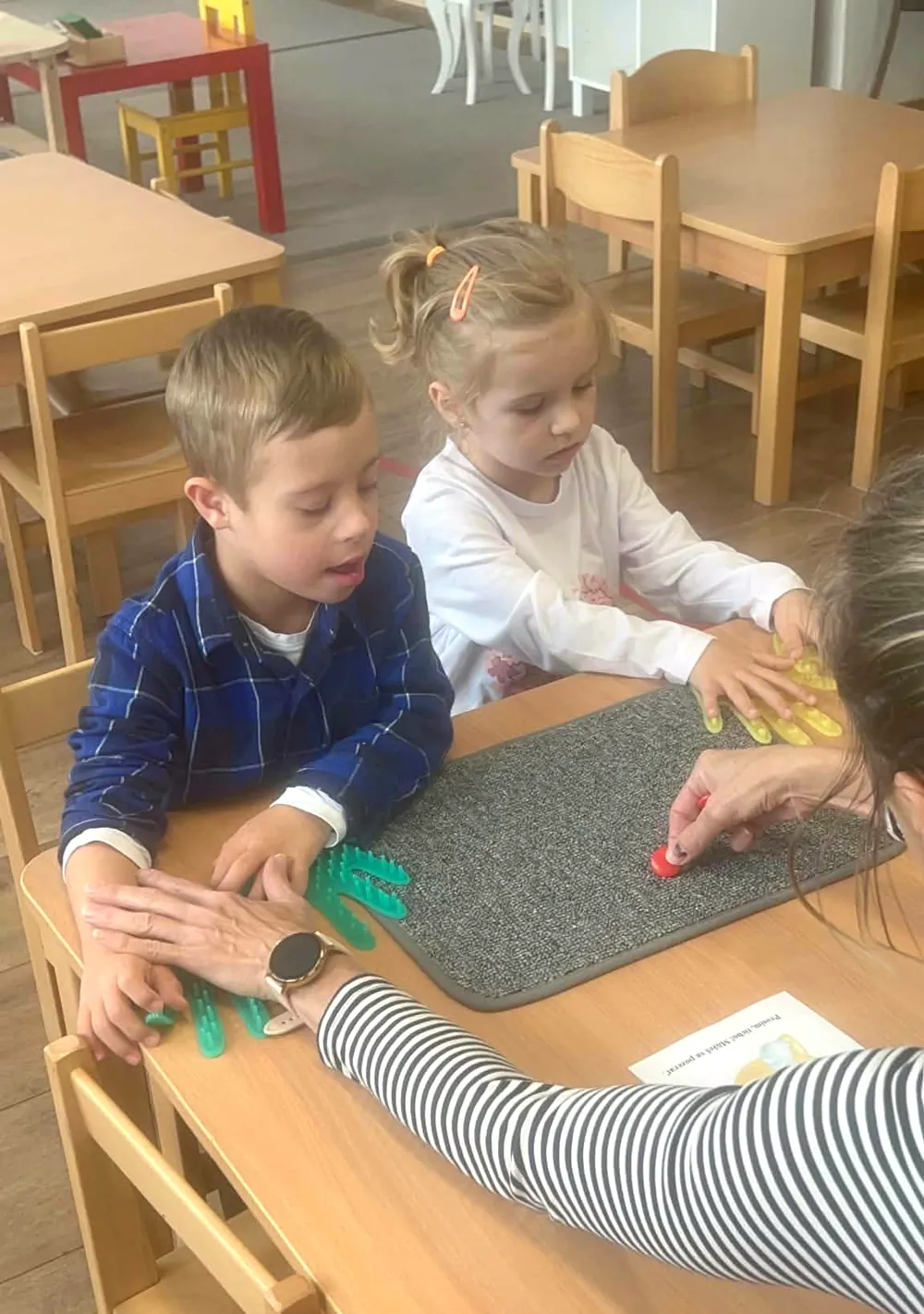 Učiteľka pracuje pri stolíku s dvoma deťmi